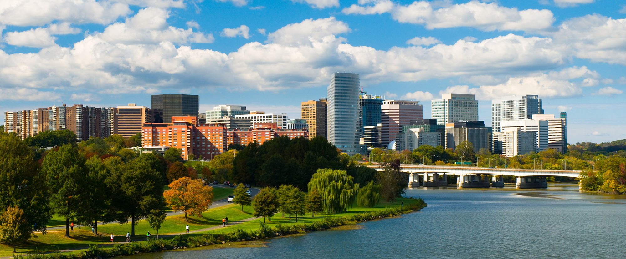 A park and river is pictured with sky scrapers and a blue sky in the background. EcoScribe provides remote deposition in Boston.