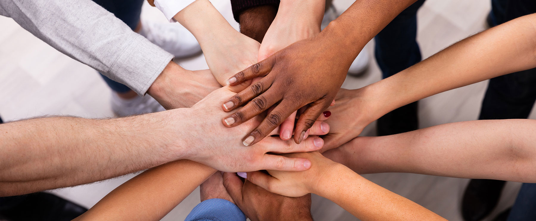 A team of professionals participate in a team building exercise with their hands in the center of the group.